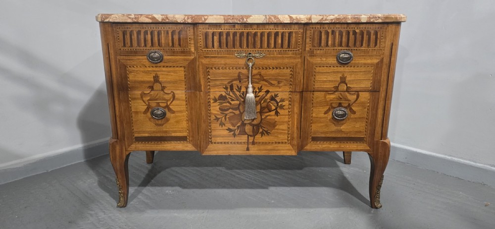 A French marquetry chest of drawers featuring inlaid urn and floral motifs, a contoured pink marble top, and cabriole legs. View IV