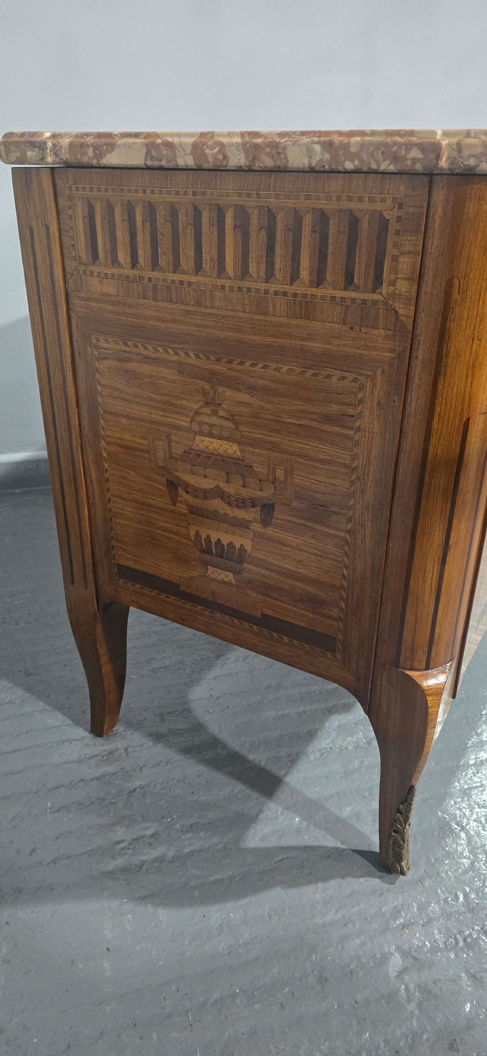 A French marquetry chest of drawers featuring inlaid urn and floral motifs, a contoured pink marble top, and cabriole legs. View VII