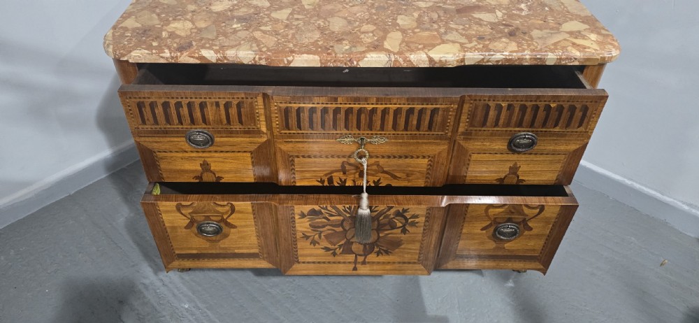 A French marquetry chest of drawers featuring inlaid urn and floral motifs, a contoured pink marble top, and cabriole legs. View XVI