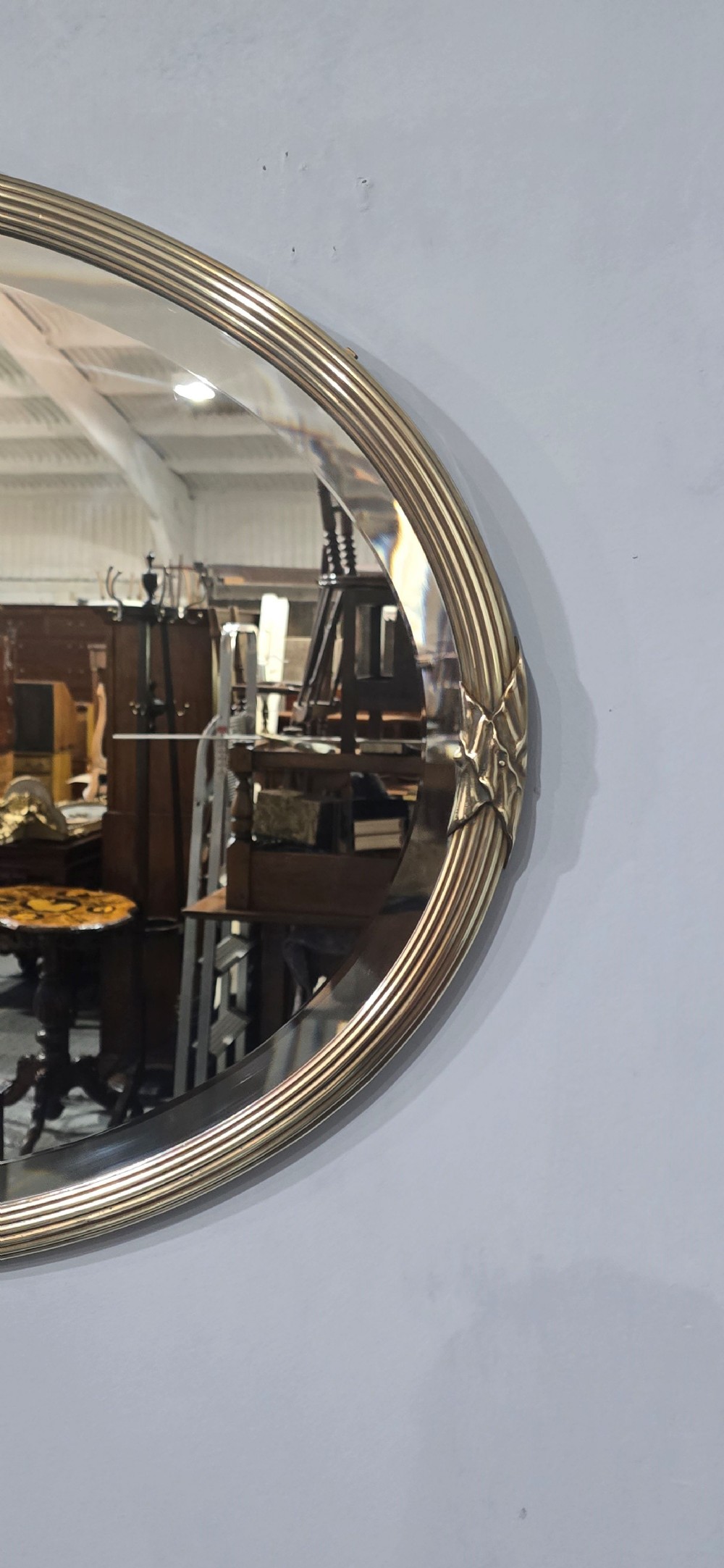 A horizontal oval Victorian brass wall mirror featuring a decorative ribbon-and-bow crest and bevelled mirror plate. View III
