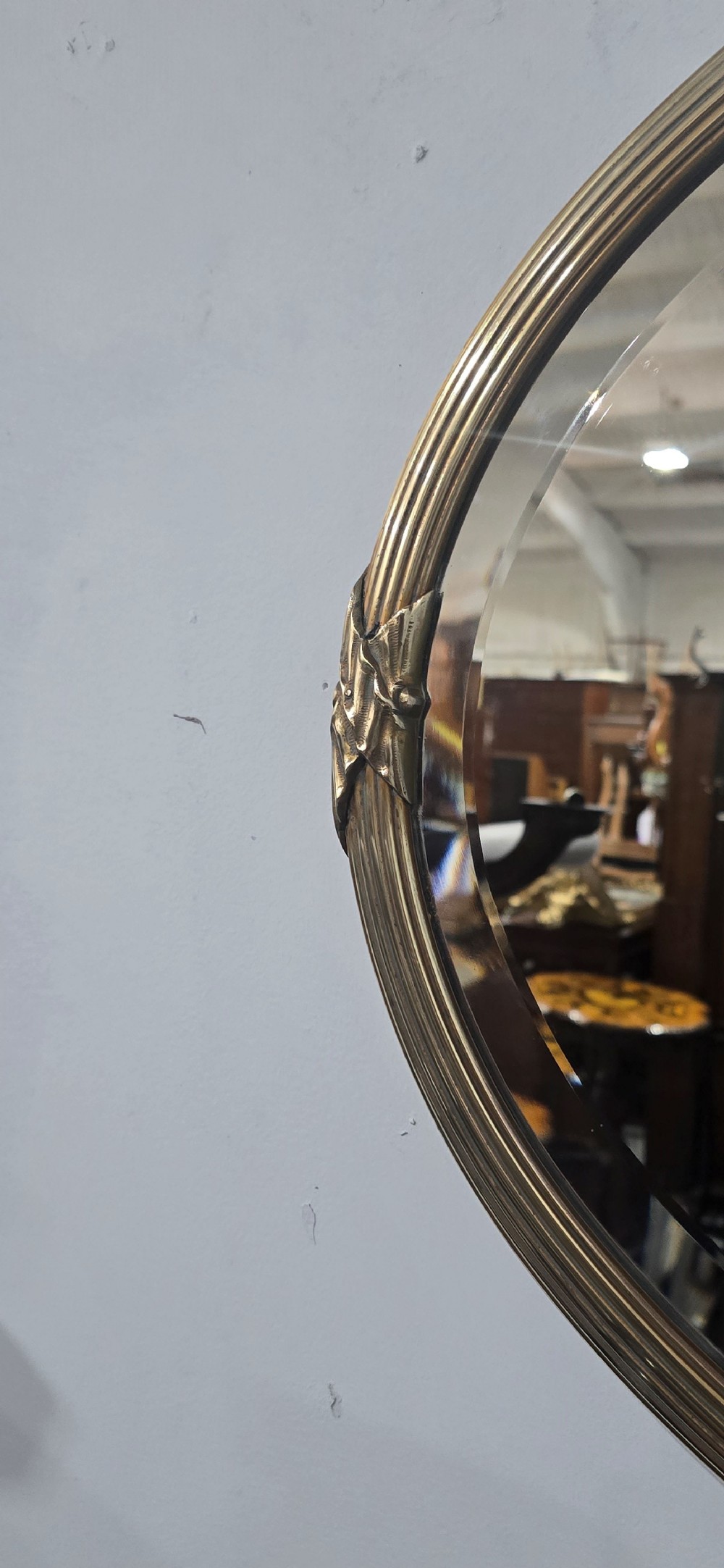 A horizontal oval Victorian brass wall mirror featuring a decorative ribbon-and-bow crest and bevelled mirror plate. View V