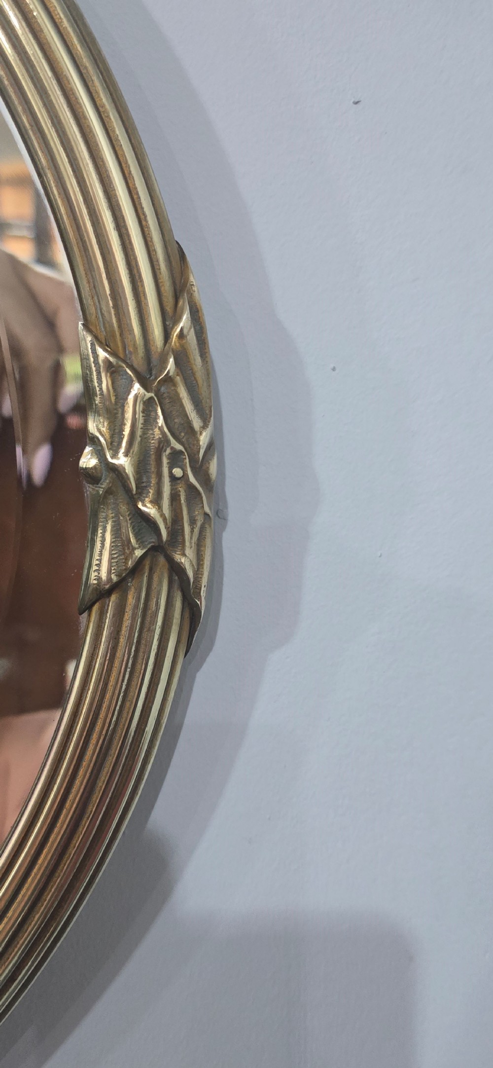 A horizontal oval Victorian brass wall mirror featuring a decorative ribbon-and-bow crest and bevelled mirror plate. View VII