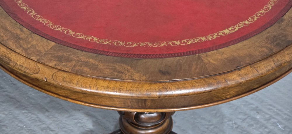A circular Victorian walnut library table featuring a reddish-brown leather inset top, turned central pedestal stem, and carved tripod legs with scroll feet. View VIII