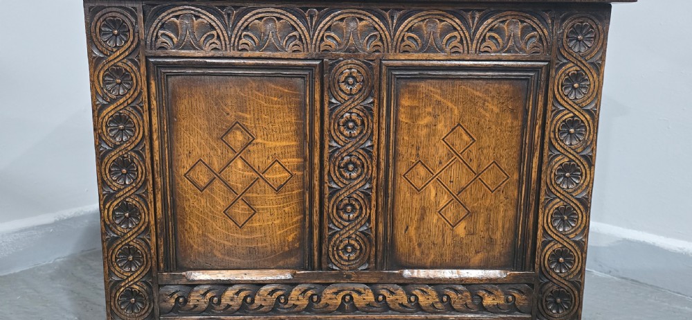 A small dark oak coffer with carved detail, geometric panel inlays, and floral guilloche borders. View V