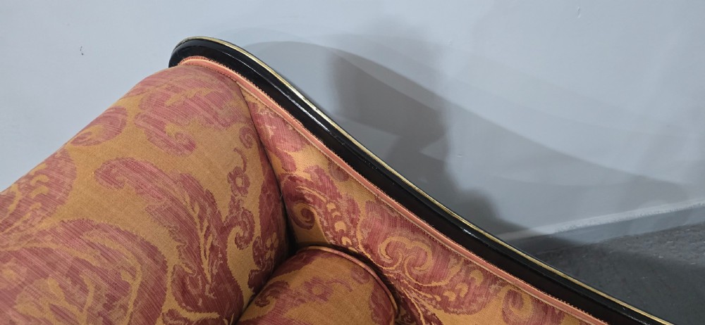An ebonised Regency chaise longue sofa with gilt details, scrolled ends, turned legs on brass castors, and patterned terracotta damask upholstery with matching bolster cushions. View VIII