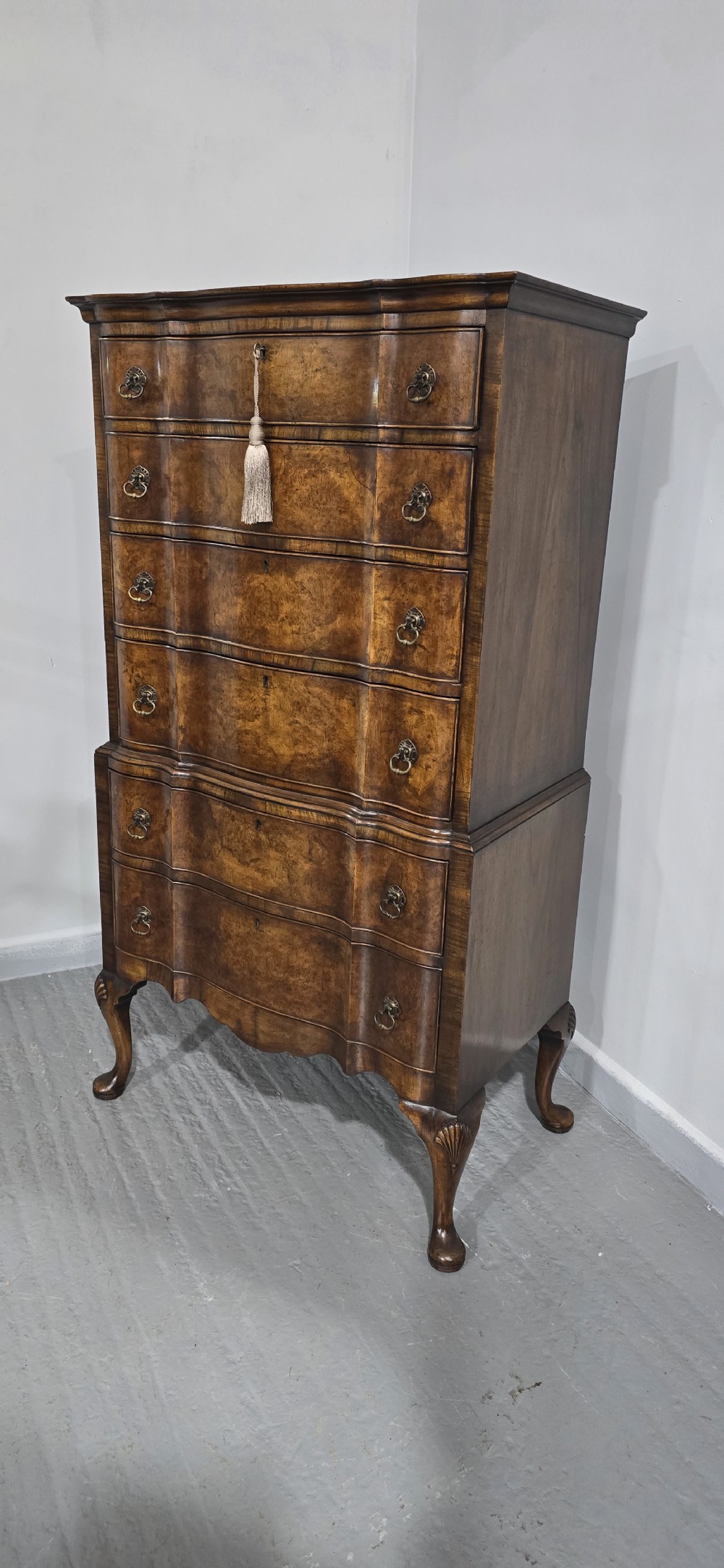 A tall Queen Anne burr walnut chest on stand featuring a serpentine contoured front with six drawers, brass drop handles, and carved cabriole legs. View III
