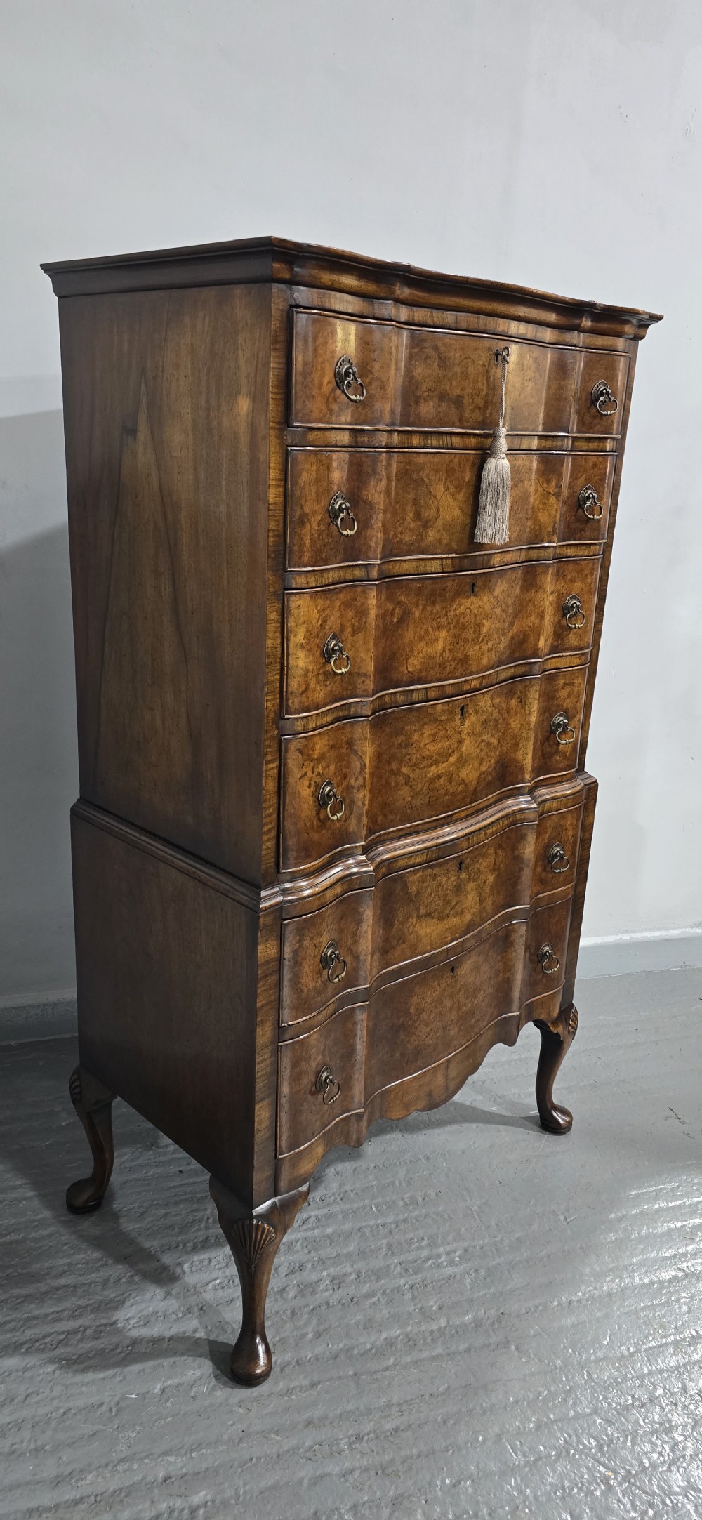 A tall Queen Anne burr walnut chest on stand featuring a serpentine contoured front with six drawers, brass drop handles, and carved cabriole legs. View IV