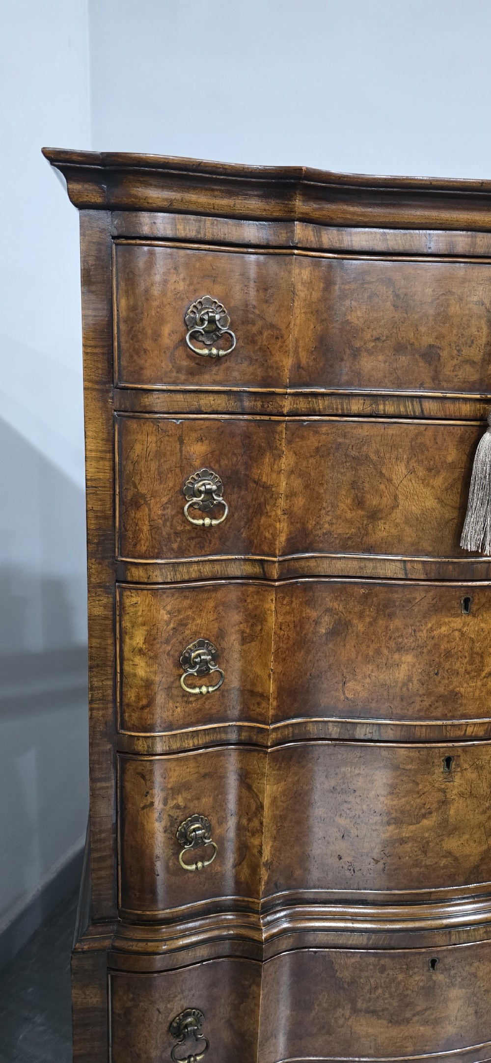 A tall Queen Anne burr walnut chest on stand featuring a serpentine contoured front with six drawers, brass drop handles, and carved cabriole legs. View V