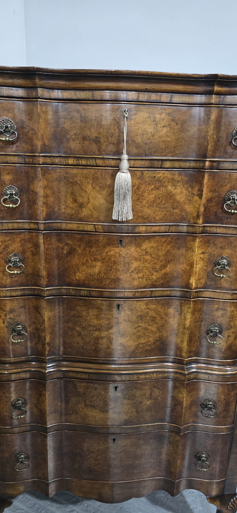 A tall Queen Anne burr walnut chest on stand featuring a serpentine contoured front with six drawers, brass drop handles, and carved cabriole legs. View VI