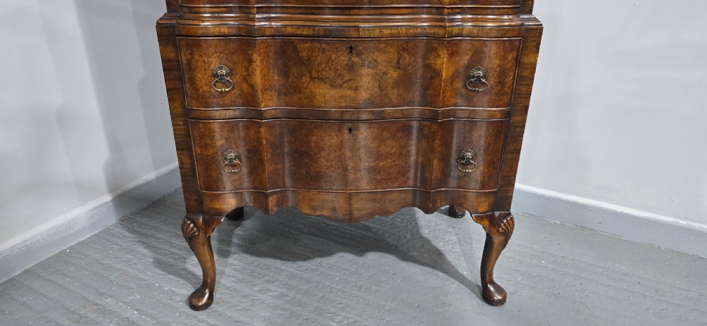 A tall Queen Anne burr walnut chest on stand featuring a serpentine contoured front with six drawers, brass drop handles, and carved cabriole legs. View VII