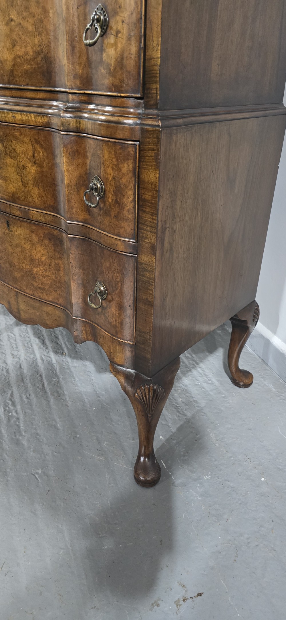 A tall Queen Anne burr walnut chest on stand featuring a serpentine contoured front with six drawers, brass drop handles, and carved cabriole legs. View VIII