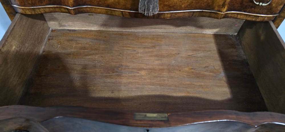 A tall Queen Anne burr walnut chest on stand featuring a serpentine contoured front with six drawers, brass drop handles, and carved cabriole legs. View IX