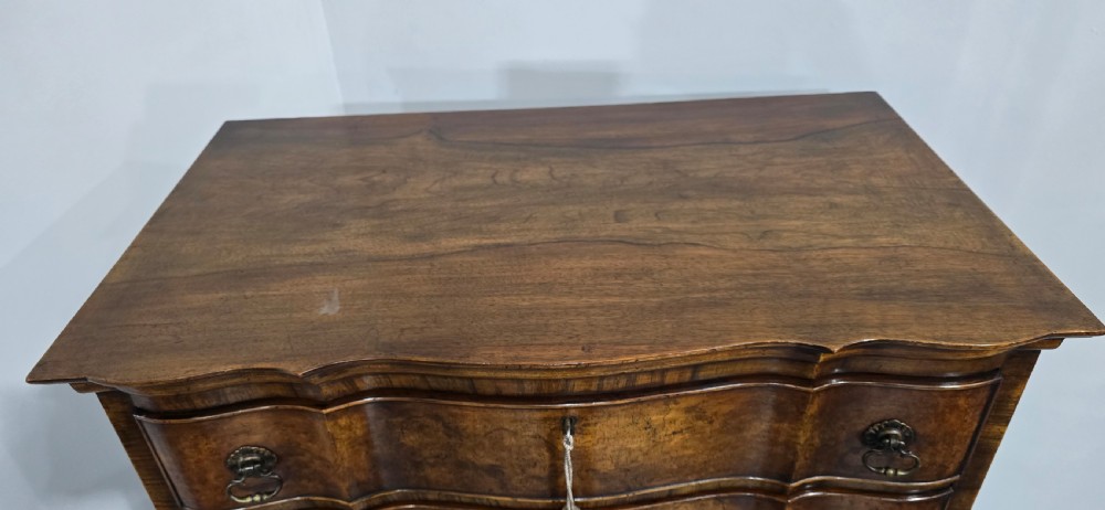 A tall Queen Anne burr walnut chest on stand featuring a serpentine contoured front with six drawers, brass drop handles, and carved cabriole legs. View XI