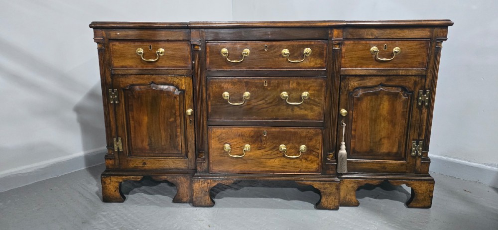 A dark oak Georgian breakfront dresser base featuring brass swan-neck handles, three central drawers, and two outer cupboard doors set on bracket feet. View III
