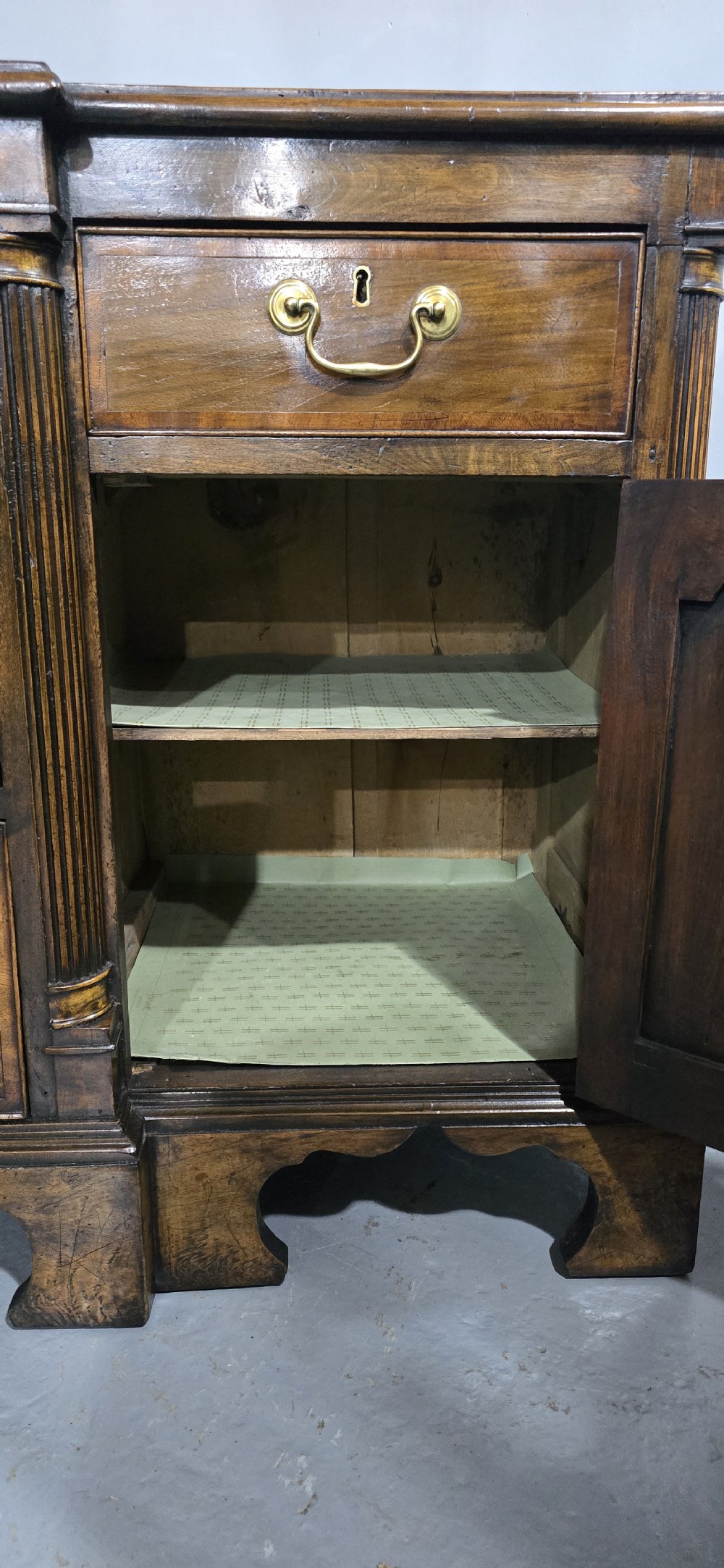 A dark oak Georgian breakfront dresser base featuring brass swan-neck handles, three central drawers, and two outer cupboard doors set on bracket feet. View X