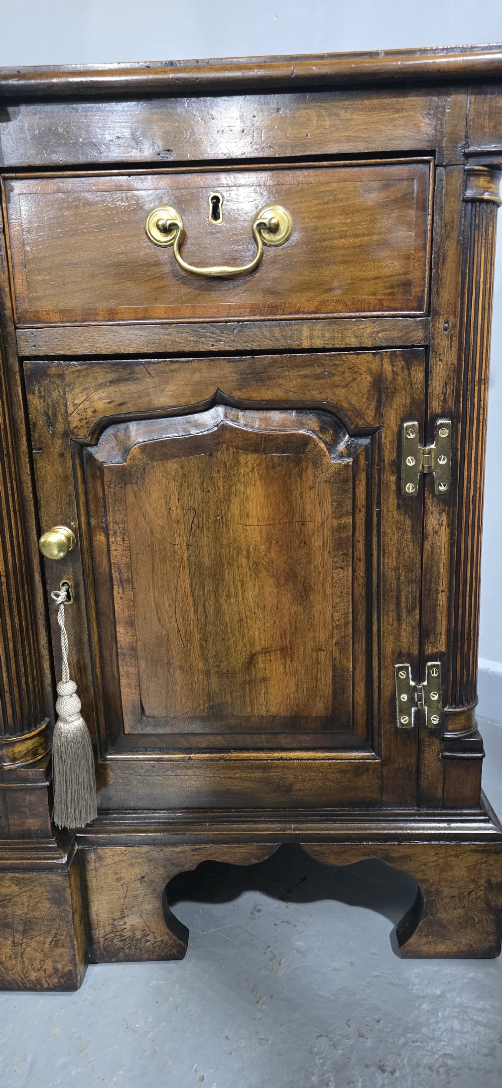 A dark oak Georgian breakfront dresser base featuring brass swan-neck handles, three central drawers, and two outer cupboard doors set on bracket feet. View XIII