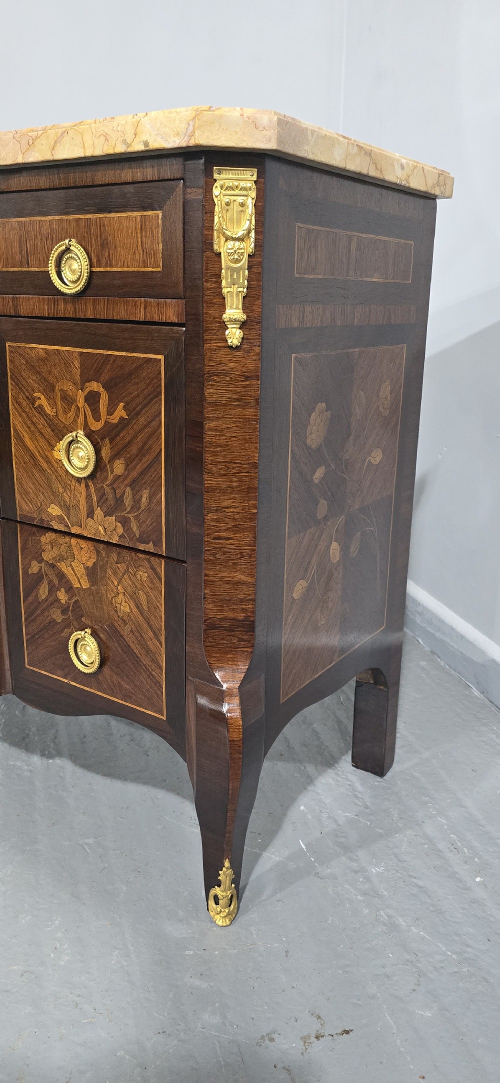 A French Louis XV style marquetry commode chest featuring floral inlays, gilt-bronze mounts, cabriole legs, and a beige marble top. View V