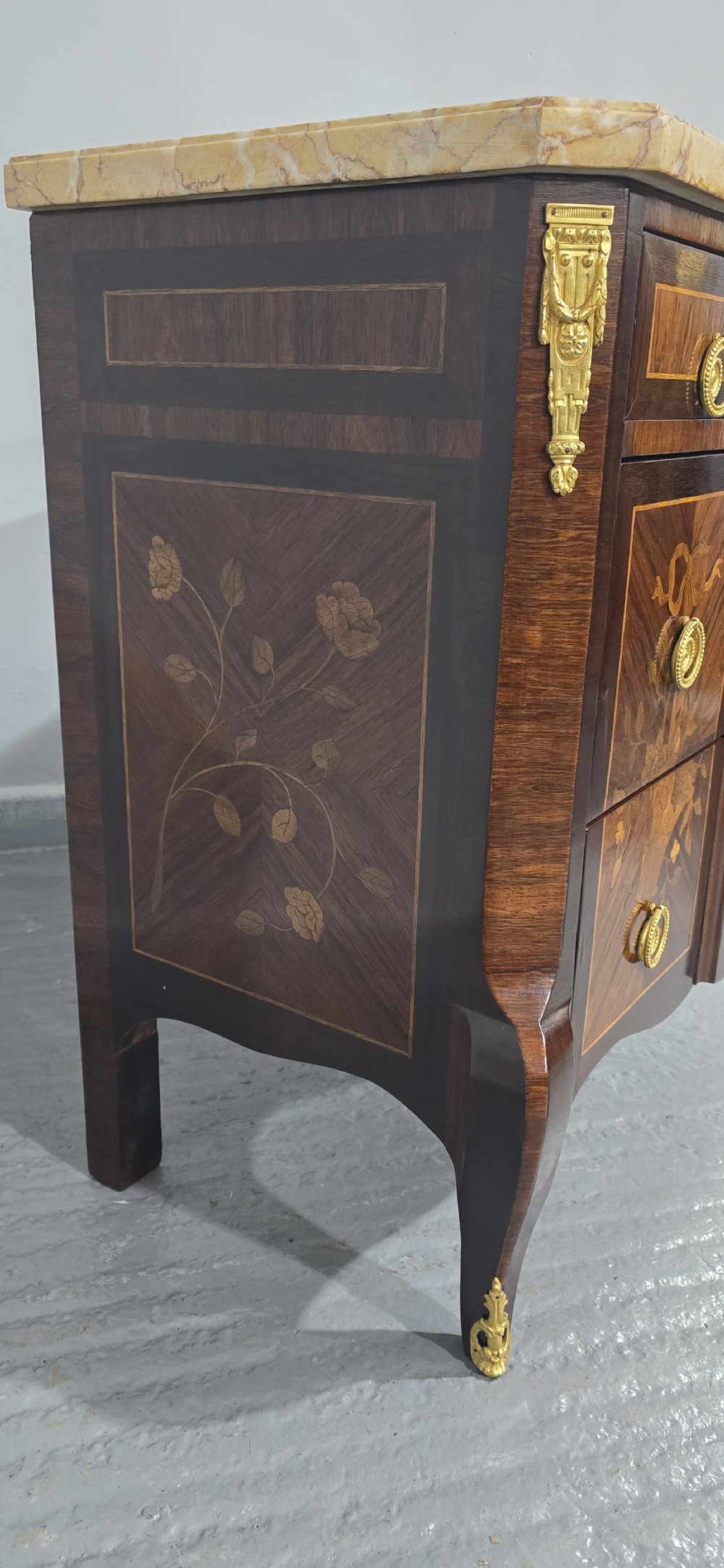 A French Louis XV style marquetry commode chest featuring floral inlays, gilt-bronze mounts, cabriole legs, and a beige marble top. View VII