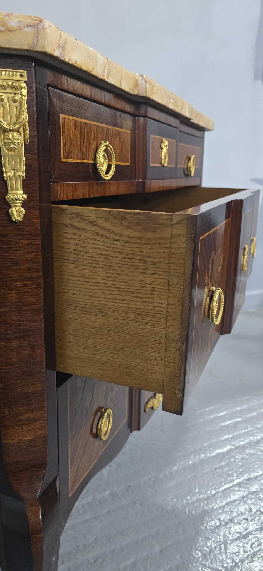 A French Louis XV style marquetry commode chest featuring floral inlays, gilt-bronze mounts, cabriole legs, and a beige marble top. View VIII