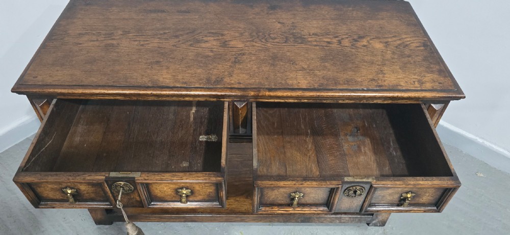 An antique dark oak dresser base featuring four panelled drawers with brass drop handles above turned supports and an open lower shelf. View VII