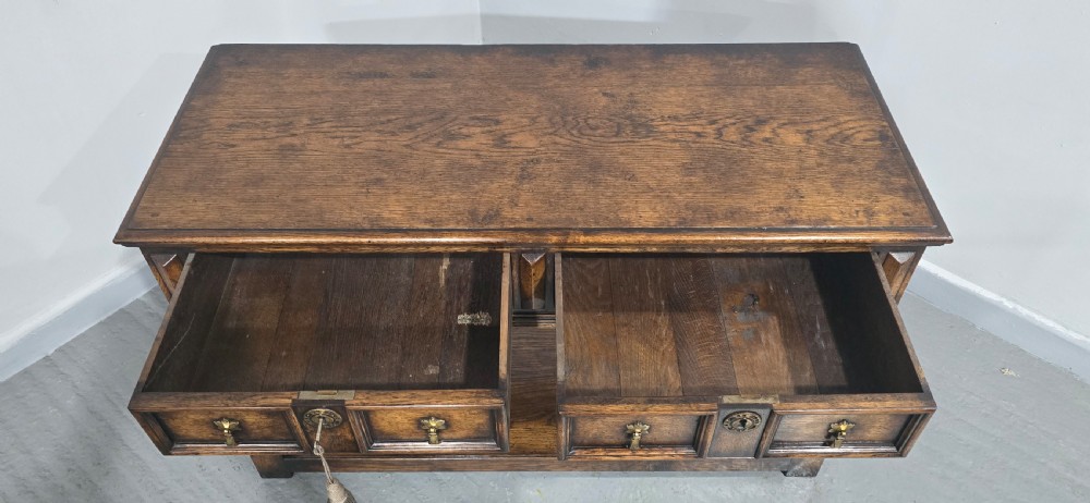 An antique dark oak dresser base featuring four panelled drawers with brass drop handles above turned supports and an open lower shelf. View VIII