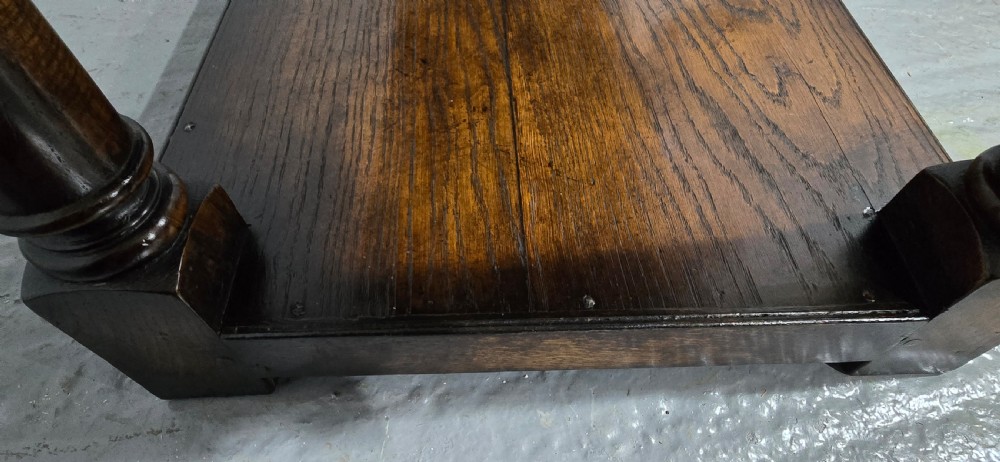 An antique dark oak dresser base featuring four panelled drawers with brass drop handles above turned supports and an open lower shelf. View XVI