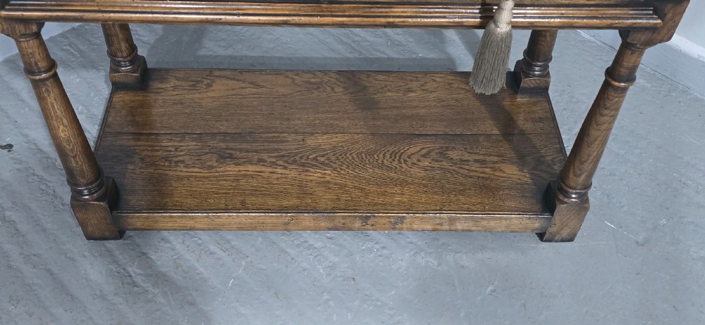 A dark oak dresser base featuring two geometric panelled drawers with brass handles, turned front legs, and a bottom shelf. View IV