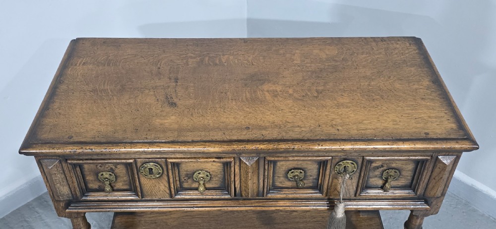 A dark oak dresser base featuring two geometric panelled drawers with brass handles, turned front legs, and a bottom shelf. View V