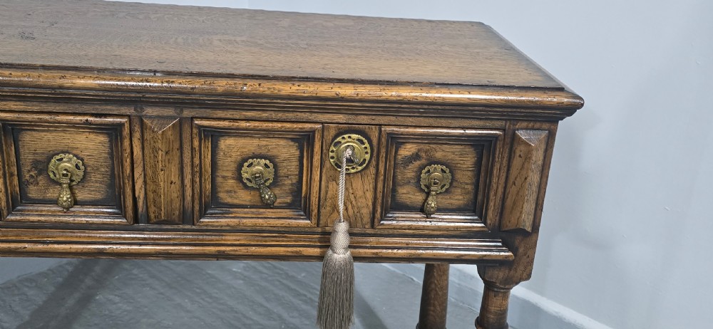 A dark oak dresser base featuring two geometric panelled drawers with brass handles, turned front legs, and a bottom shelf. View VI
