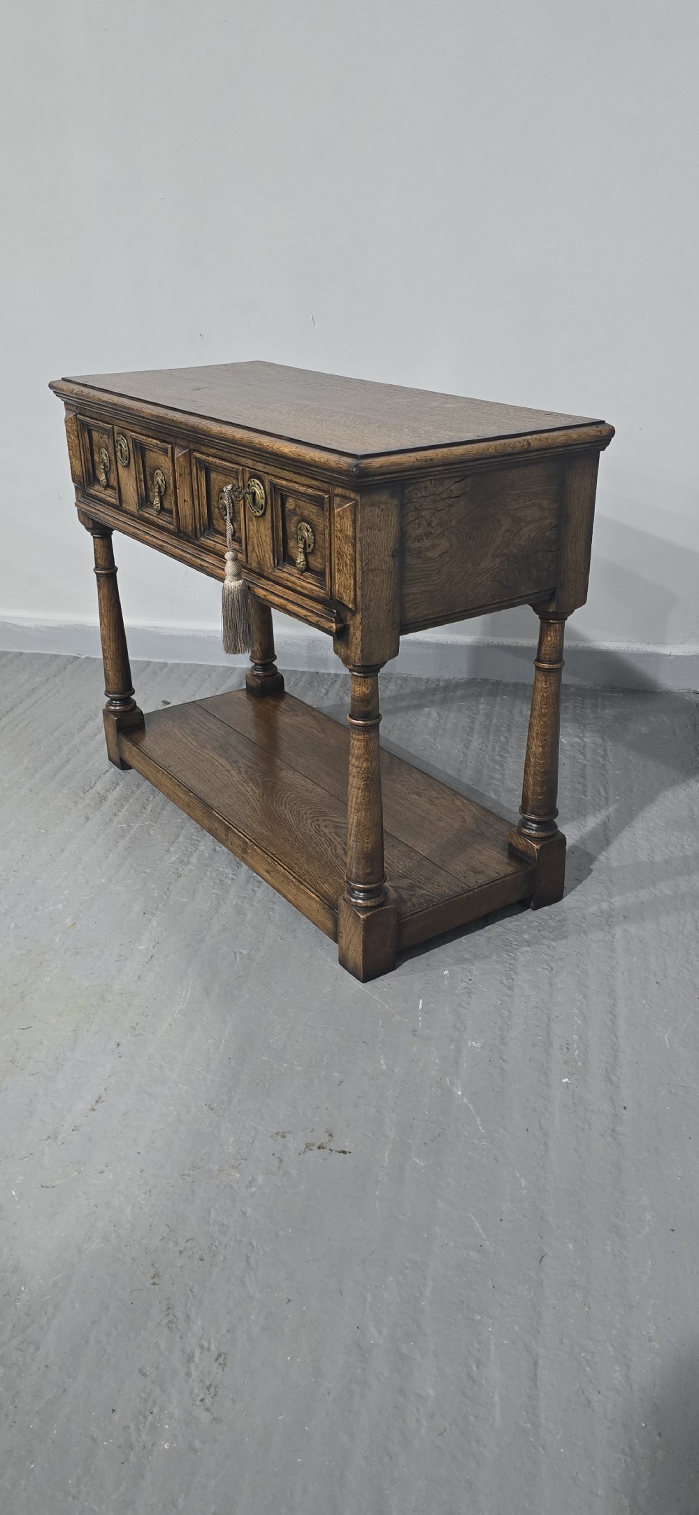 A dark oak dresser base featuring two geometric panelled drawers with brass handles, turned front legs, and a bottom shelf. View VIII