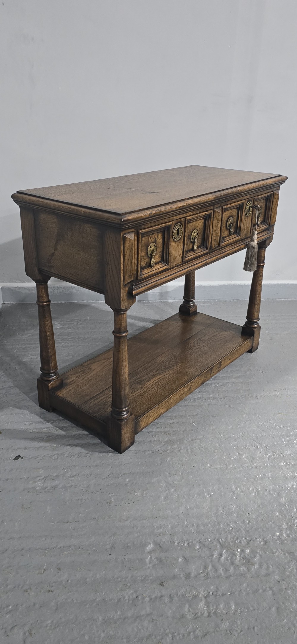 A dark oak dresser base featuring two geometric panelled drawers with brass handles, turned front legs, and a bottom shelf. View IX