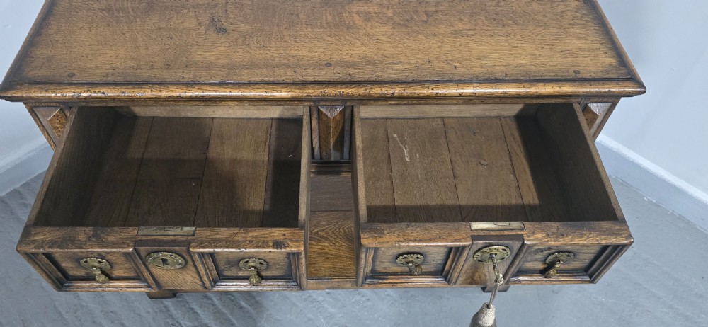 A dark oak dresser base featuring two geometric panelled drawers with brass handles, turned front legs, and a bottom shelf. View X