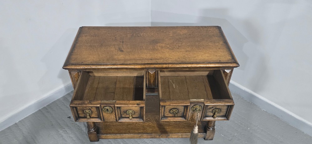 A dark oak dresser base featuring two geometric panelled drawers with brass handles, turned front legs, and a bottom shelf. View XI