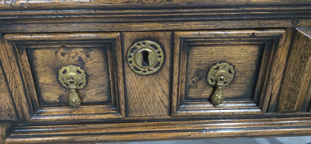 A dark oak dresser base featuring two geometric panelled drawers with brass handles, turned front legs, and a bottom shelf. View XII
