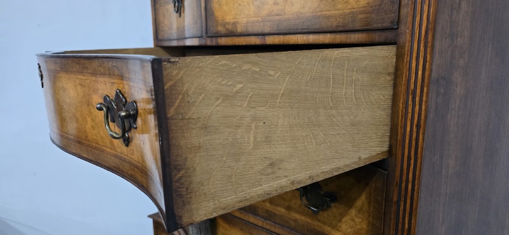 A tall two-part burr walnut chest on chest featuring a curved serpentine front, multi-drawer arrangement with brass drop handles, and bracket feet. View IX