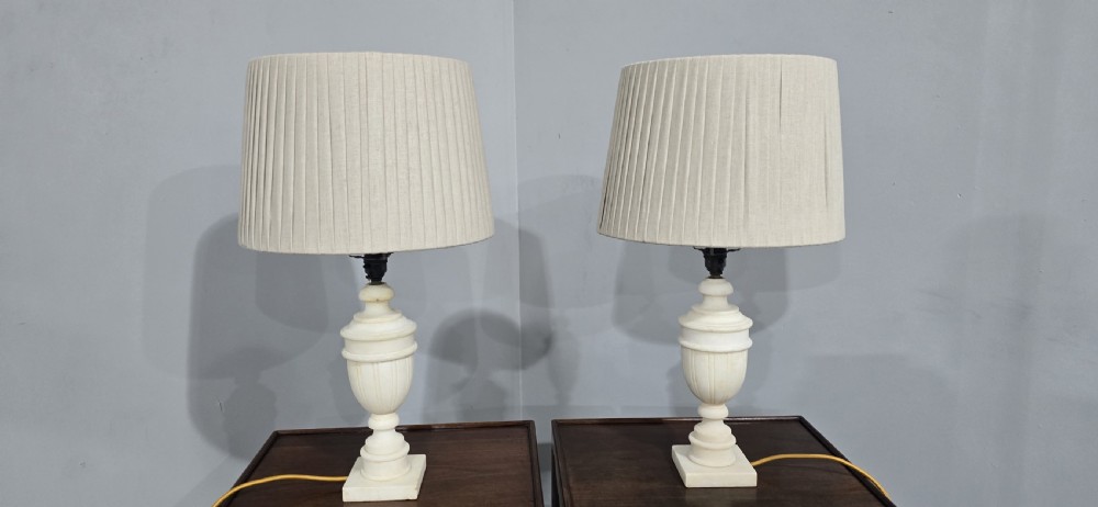 A pair of carved off-white marble urn-form table lamps with square plinth bases and pleated cream fabric shades. View VI