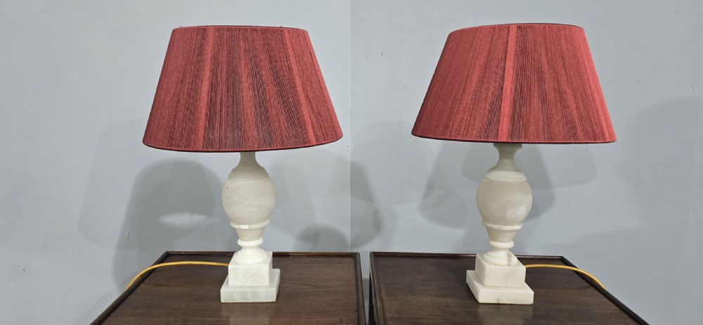 A pair of carved cream marble table lamps featuring urn-shaped stems on square plinth bases with pleated red fabric shades. View III