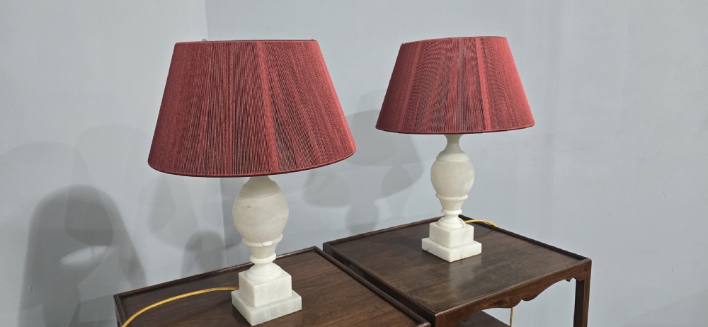 A pair of carved cream marble table lamps featuring urn-shaped stems on square plinth bases with pleated red fabric shades. View V