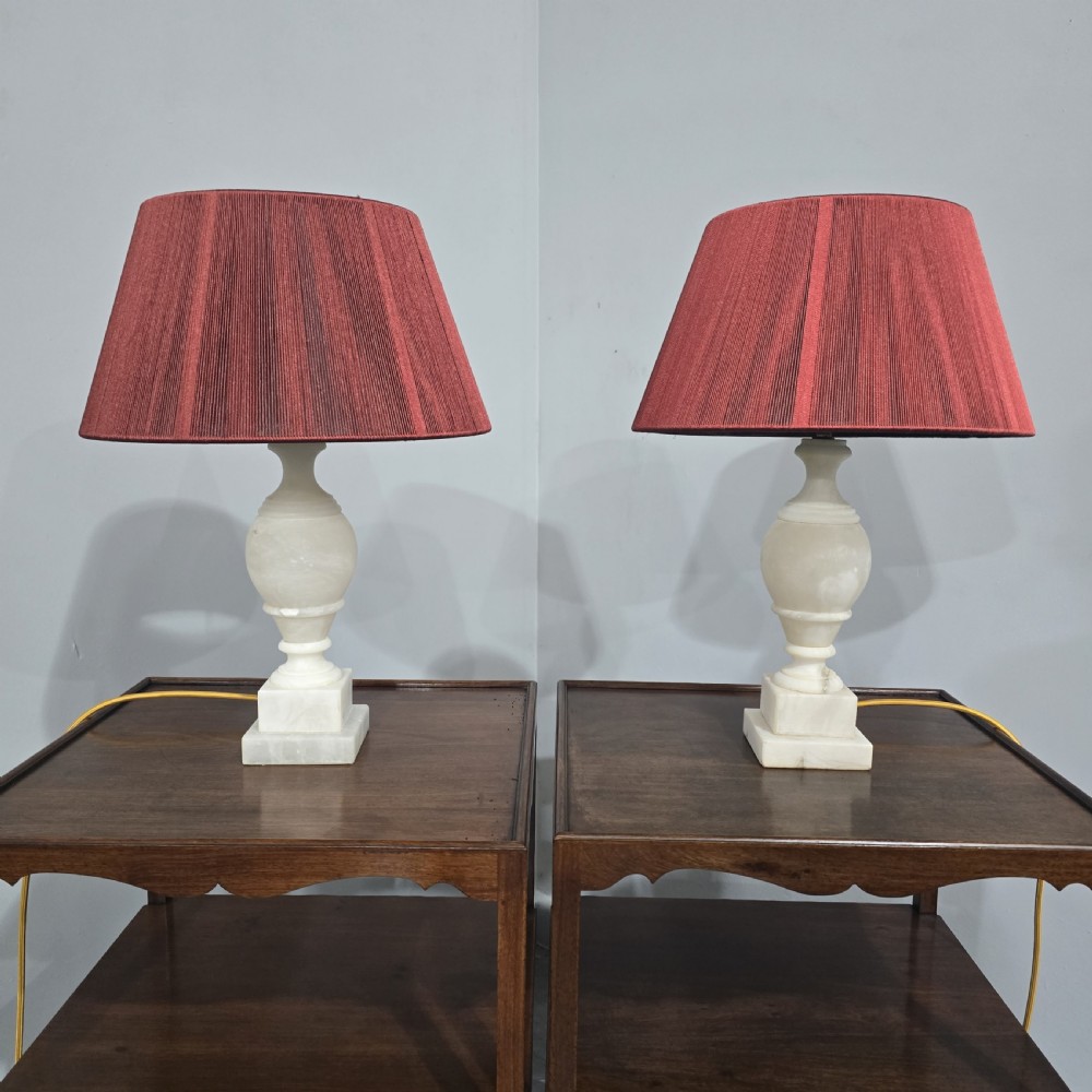 A pair of carved cream marble table lamps featuring urn-shaped stems on square plinth bases with pleated red fabric shades. View VII