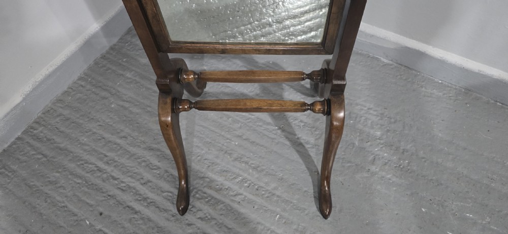 A standing Queen Anne style walnut cheval mirror with an arched moulded frame, adjustable brass tilt controls, and shaped splayed legs joined by turned stretchers. View VI