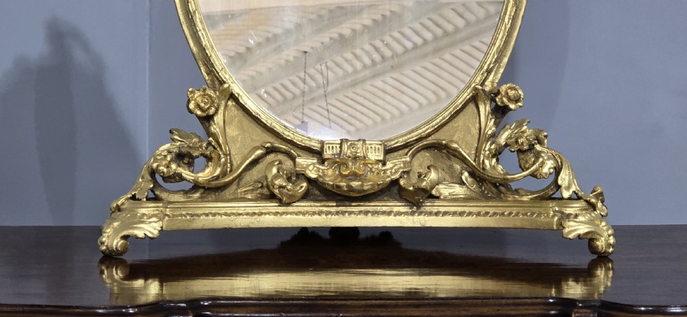 An oval gilt metal dressing table mirror with a top floral wreath cresting and an acanthus leaf scroll base. View III