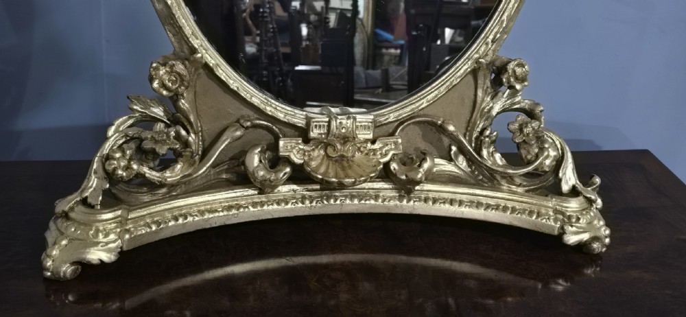 An oval gilt metal dressing table mirror with a top floral wreath cresting and an acanthus leaf scroll base. View VI