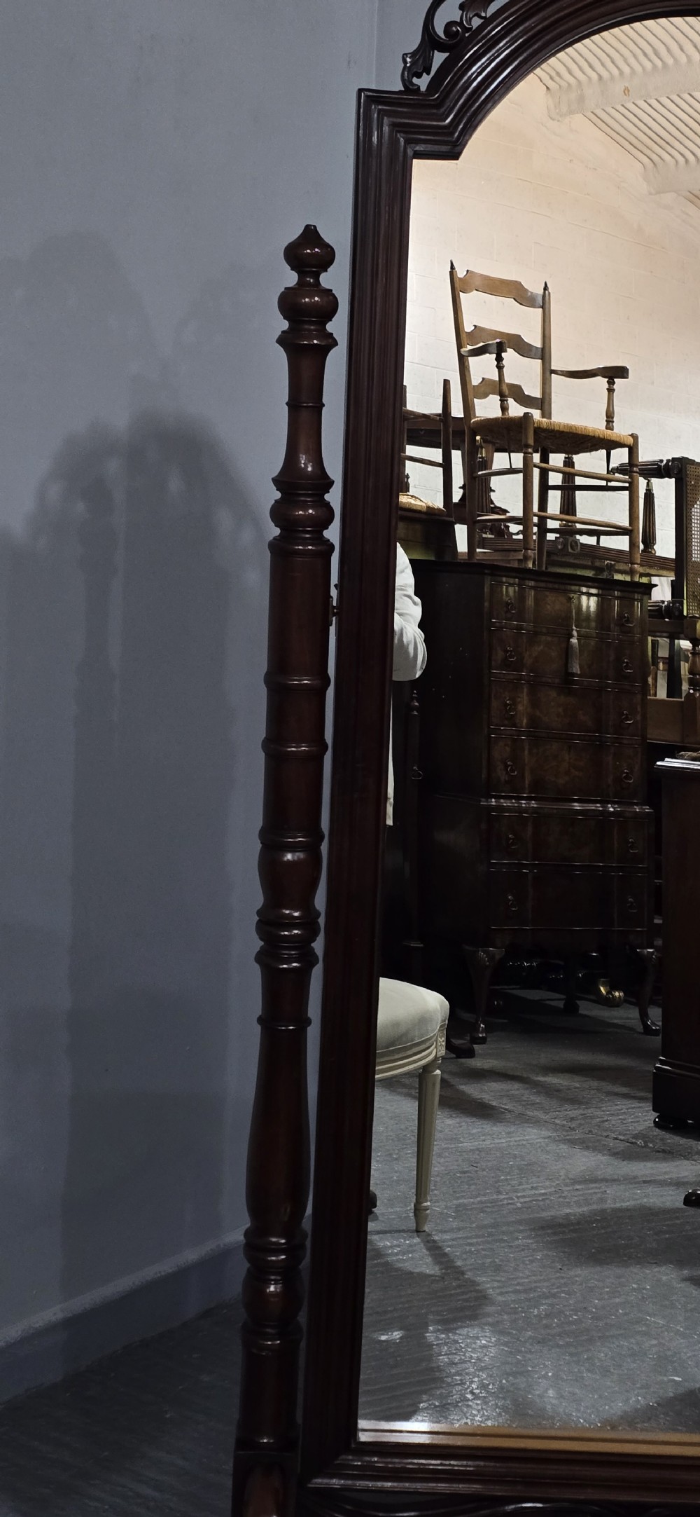 A tall mahogany cheval mirror featuring an arched frame topped with a carved scrollwork crest, mounted between two turned posts on splayed legs. View V