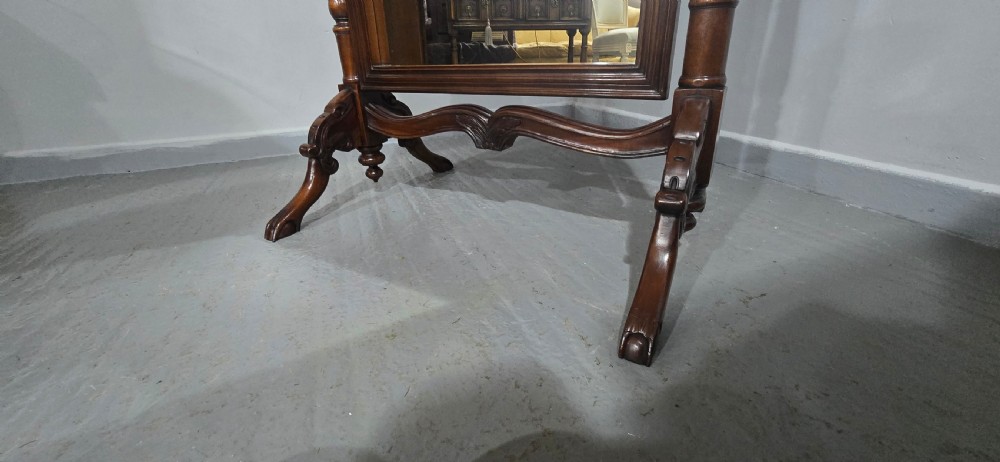A tall mahogany cheval mirror featuring an arched frame topped with a carved scrollwork crest, mounted between two turned posts on splayed legs. View XII