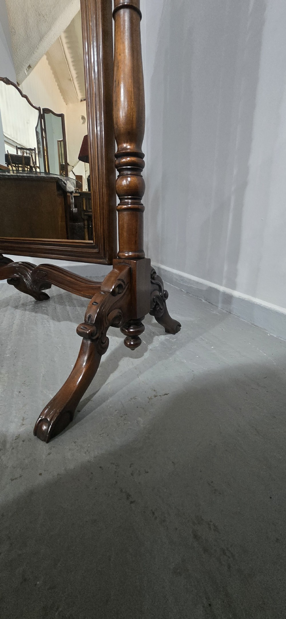A tall mahogany cheval mirror featuring an arched frame topped with a carved scrollwork crest, mounted between two turned posts on splayed legs. View XIII