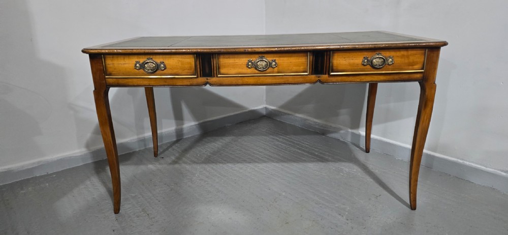 A French style warm oak library desk featuring a green leather inset writing surface, three frieze drawers with decorative brass handles, and slender cabriole legs. View III
