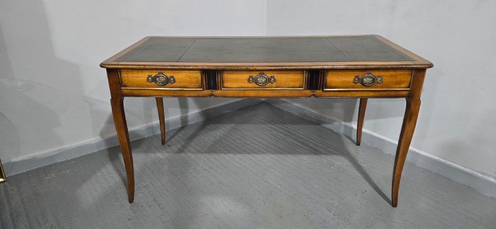 A French style warm oak library desk featuring a green leather inset writing surface, three frieze drawers with decorative brass handles, and slender cabriole legs. View IV