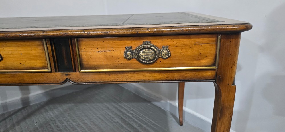 A French style warm oak library desk featuring a green leather inset writing surface, three frieze drawers with decorative brass handles, and slender cabriole legs. View V