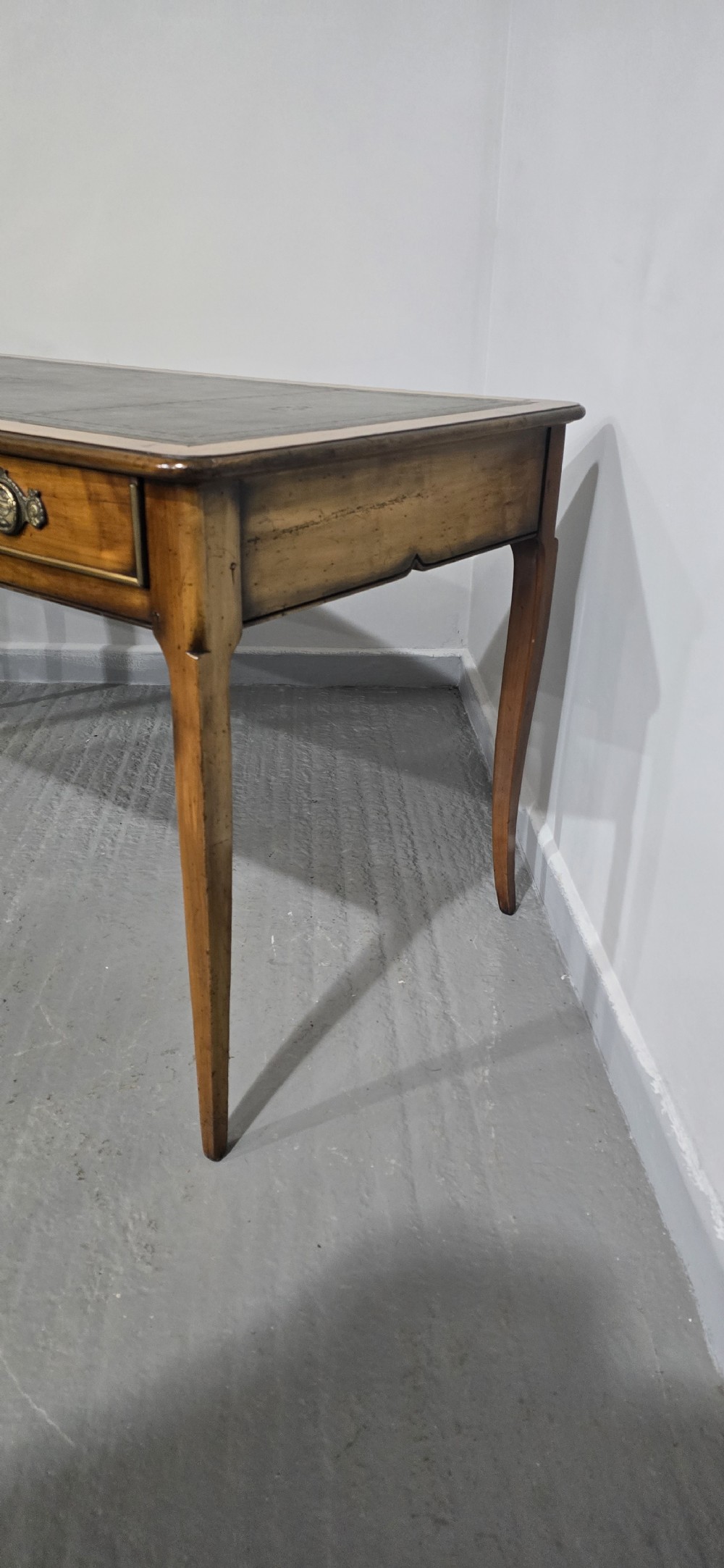 A French style warm oak library desk featuring a green leather inset writing surface, three frieze drawers with decorative brass handles, and slender cabriole legs. View VI