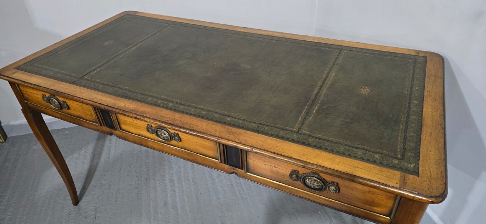 A French style warm oak library desk featuring a green leather inset writing surface, three frieze drawers with decorative brass handles, and slender cabriole legs. View VII